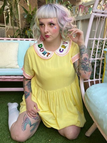girl wearing yellow dress with pink trimmed sleeves and collar. collar reads "Don't cry"